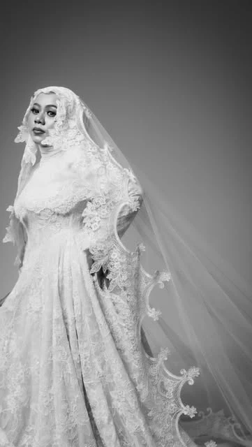 Potret hitam putih pengantin perempuan mengenakan gaun dengan ekor kain berenda